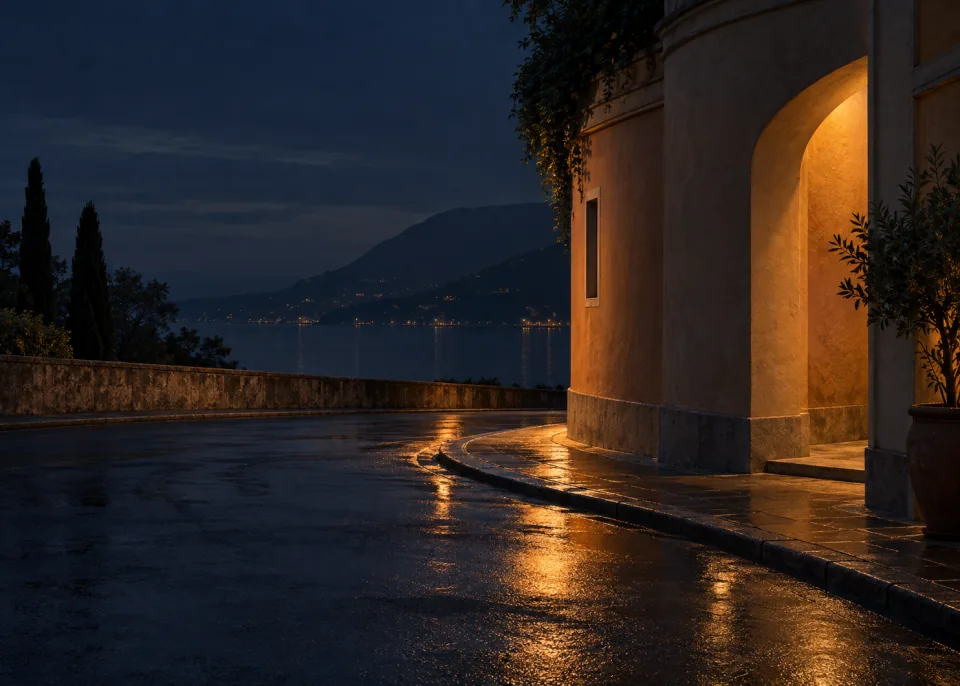 Amber Corner: A quiet rounded stucco street corner lit by a concealed warm amber lamp, smooth charcoal background and wet pavement reflection in lower half.