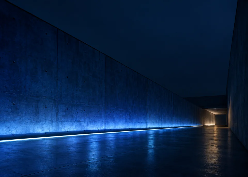 Indigo Passage: An empty minimal concrete passage with broad deep indigo illumination along one side and soft dark blue upper wall, vanishing point low right.