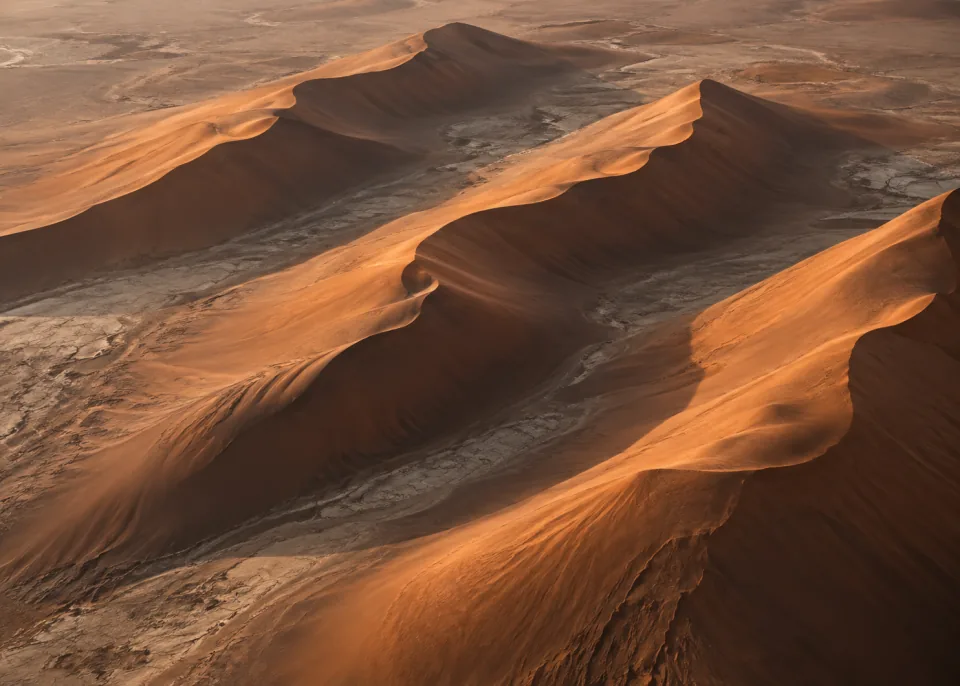 Copper Ridges: Oblique aerial of three long parallel copper-colored dune ridges, rich soft brown shadows, spacious diagonal composition.