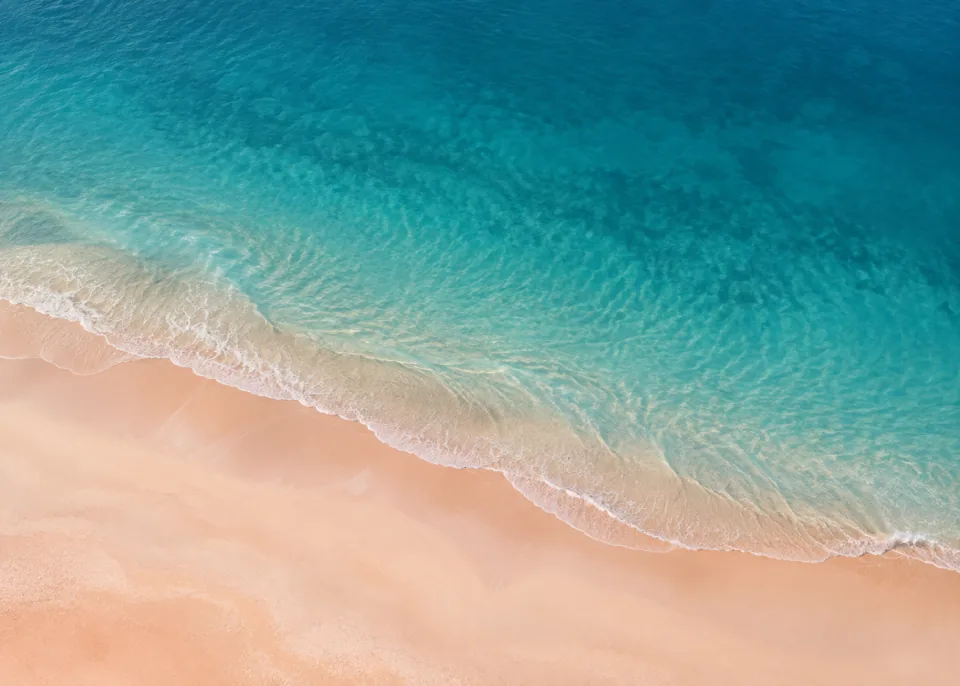 Coral Sand: Dusty warm coral-beige sand meets desaturated turquoise sea in one diagonal curve across lower half, faint smooth wave wash with no froth clutter.