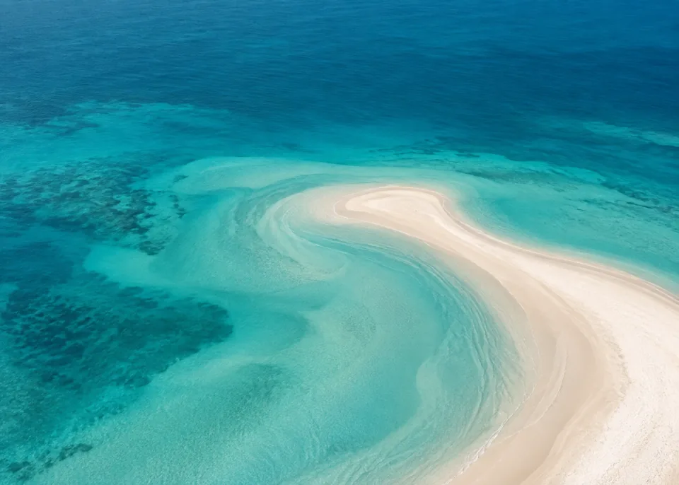 Turquoise Crescent: A broad ivory sandbar crescent enters from lower right into spacious muted turquoise shallows and deeper teal upper water.