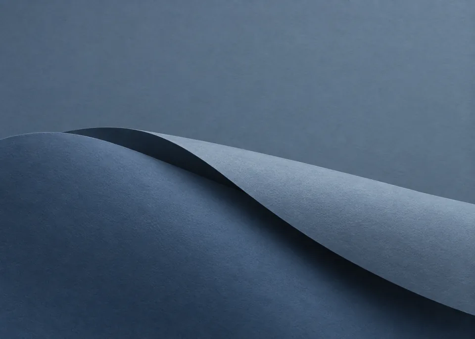 Blue Pleat: Two broad asymmetrical blue-gray folded paper planes overlap along a soft diagonal in lower half, cool slate background and gentle blue shadows.