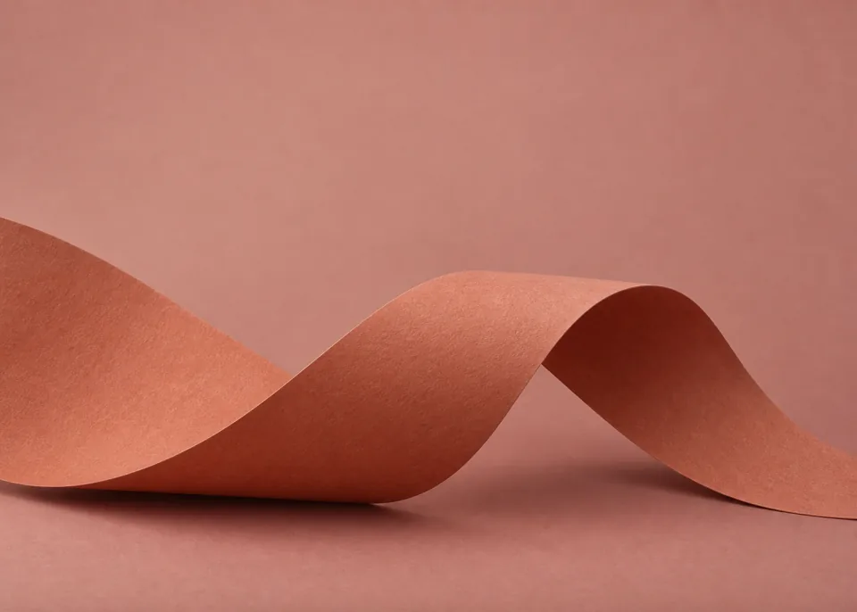 Terracotta Curl: A single wide muted terracotta paper strip curls gently through lower center without closing into a ring, dusty rose backdrop.