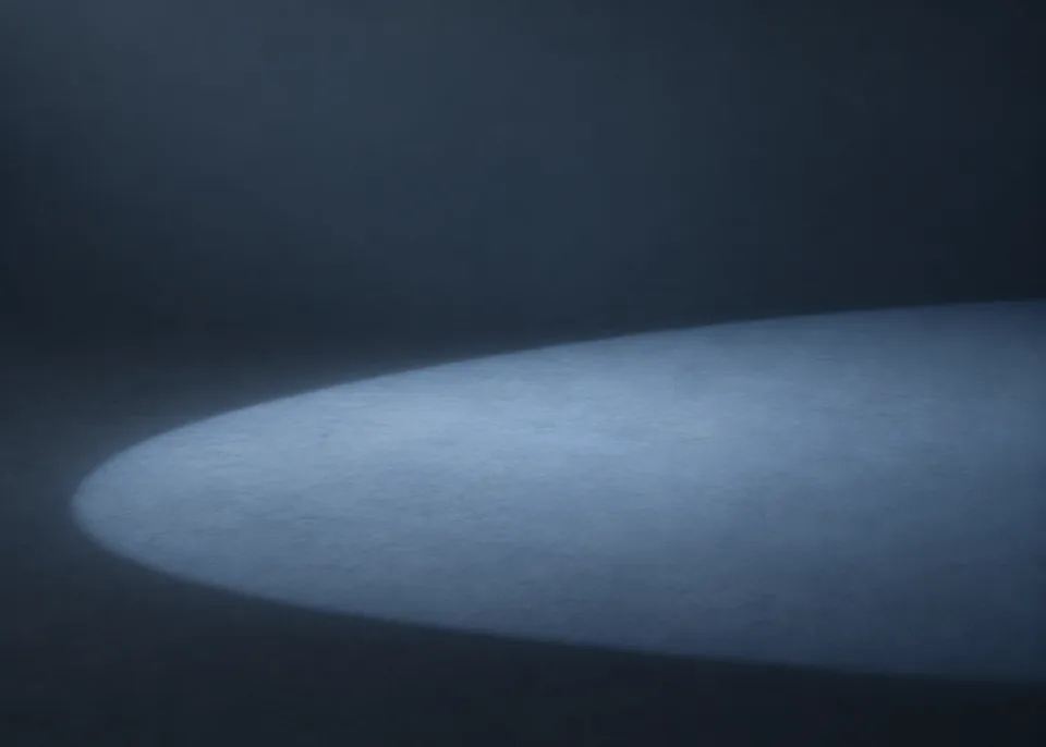 Blue Aperture: A large off-center ellipse of desaturated blue light crosses the lower half of a deep slate matte surface, subtly blurred falloff, no literal hole.